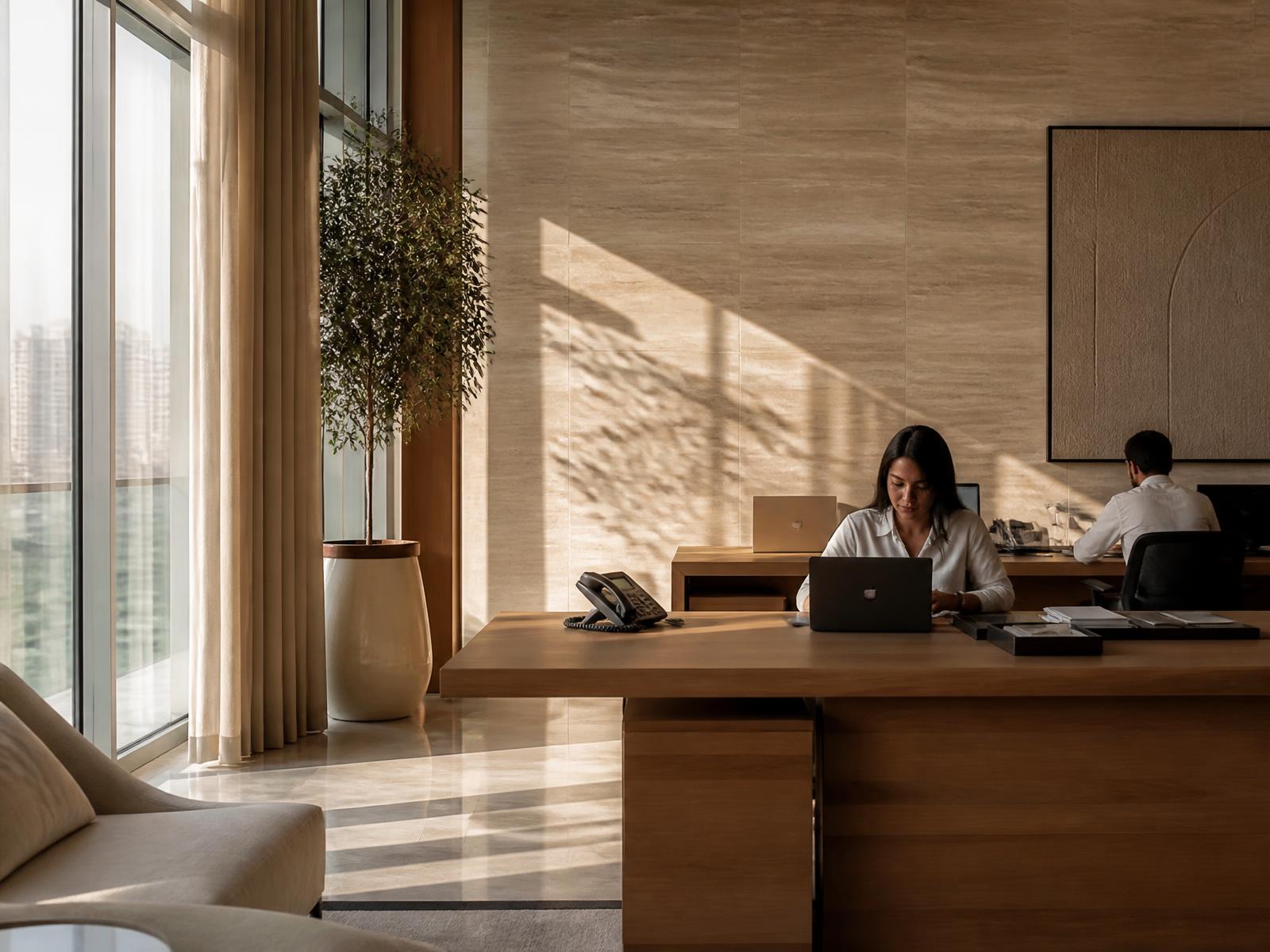 A warm modern office interior with oak desks, travertine walls, and soft daylight